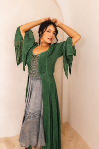 Woman wearing a green dress with a textured pattern over a gray dress against a neutral background